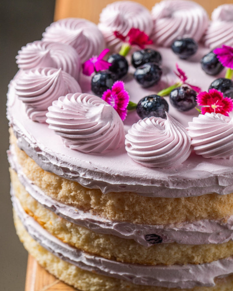 Layered cake with pink frosting and berries on a wooden stand